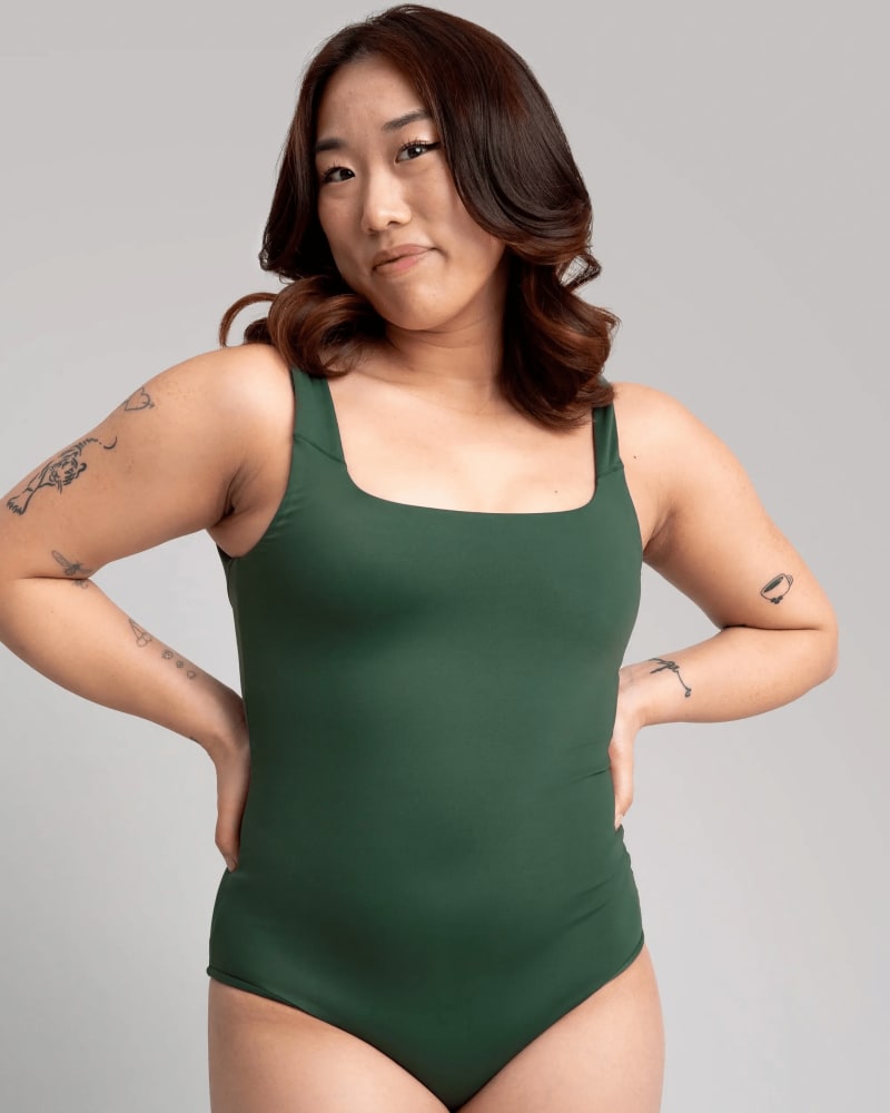 Front of a model wearing a size 5X surf's up swim one piece in sycamore green by alder apparel. | dia_product_style_image_id:296831